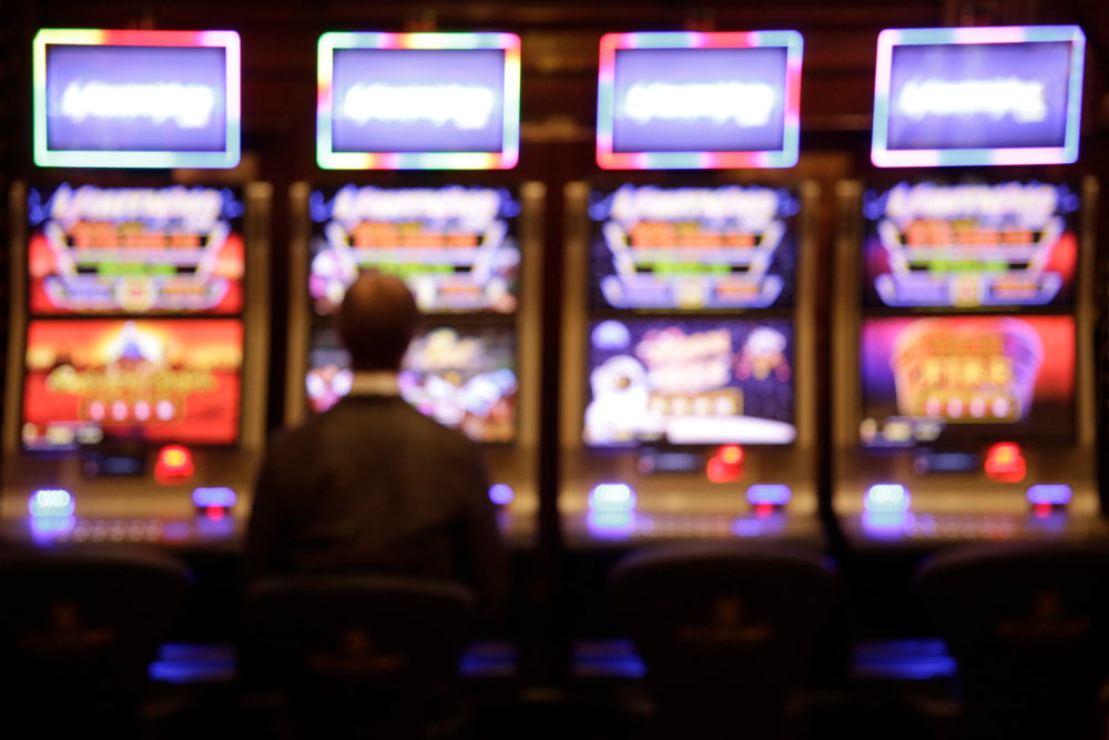 Man,In,Front,Of,Four,Brightly,Lit,Slot,Machines,In