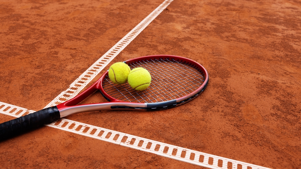 Tennis,Racket,With,Two,Balls,On,Clay,Court